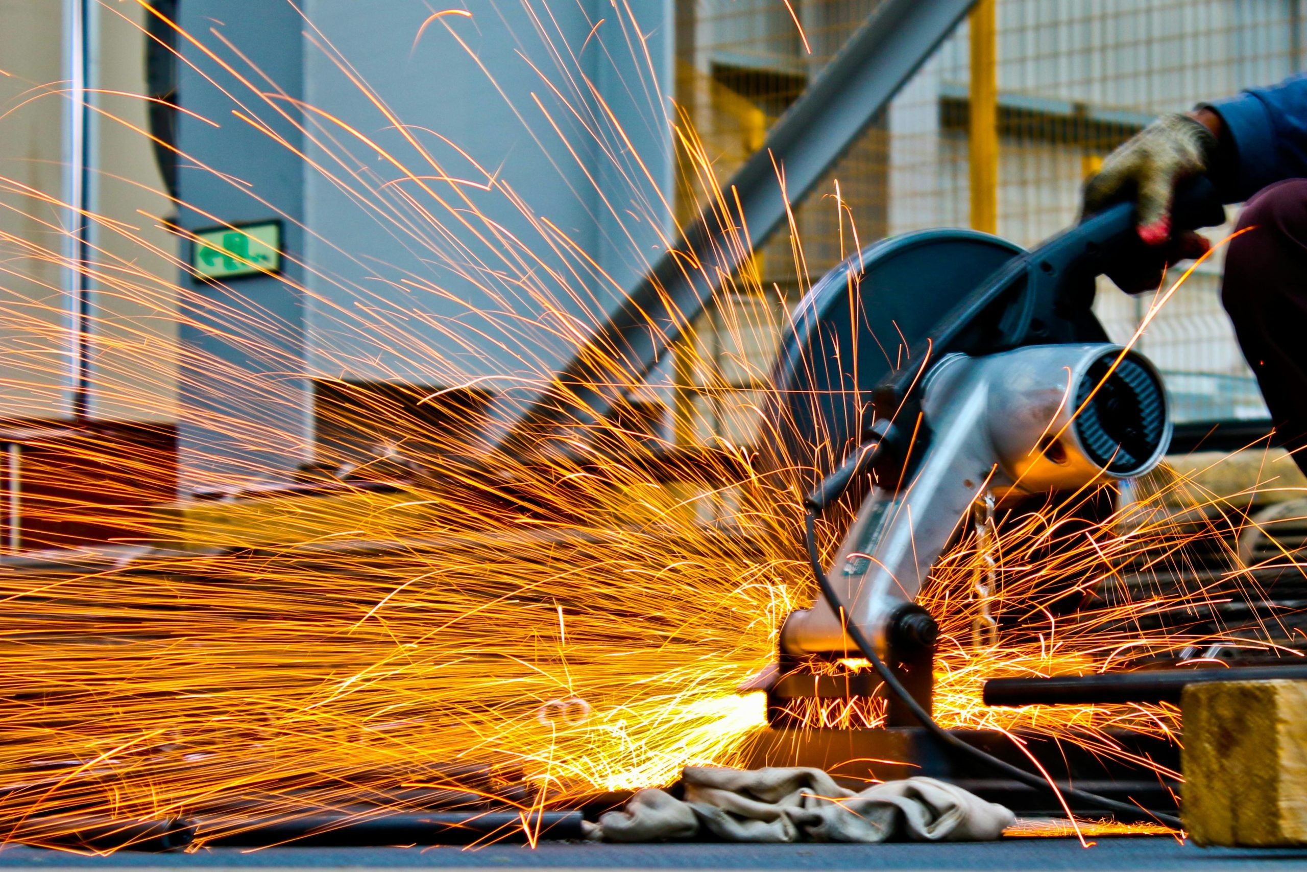Industrial worker using a cutting tool with sparks flying during metal fabrication in a defense engineering facility.